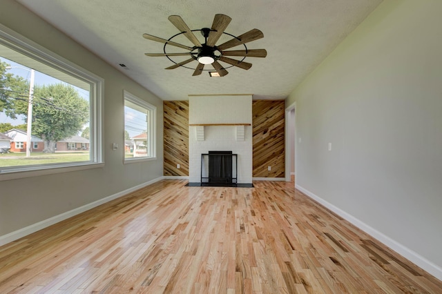 unfurnished living room featuring a brick fireplace, a textured ceiling, wooden walls, and light hardwood / wood-style flooring