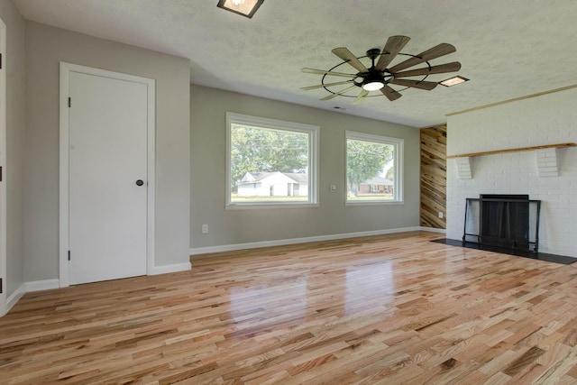 unfurnished living room featuring ceiling fan, a fireplace, light hardwood / wood-style flooring, and a textured ceiling