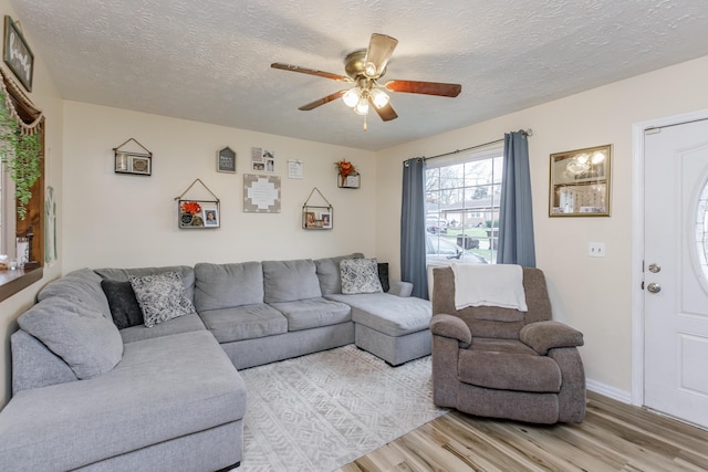 living room featuring ceiling fan, a textured ceiling, and light wood-type flooring