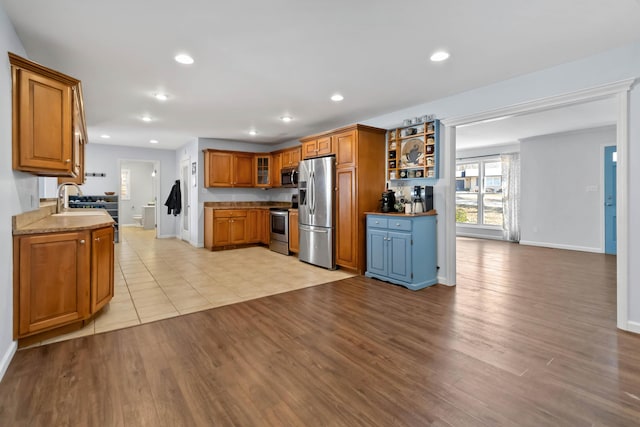 kitchen with light stone countertops, appliances with stainless steel finishes, sink, and light hardwood / wood-style floors