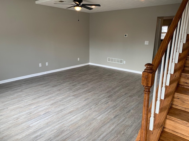 empty room featuring ceiling fan, dark wood-style flooring, visible vents, baseboards, and stairway