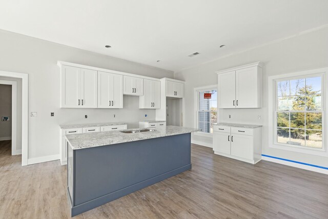 kitchen featuring white cabinetry, light stone counters, a kitchen island with sink, and light wood-type flooring