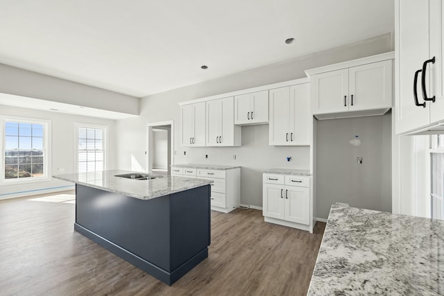 kitchen with white cabinetry, wood-type flooring, light stone countertops, and an island with sink