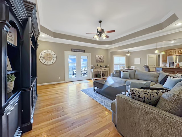 living room featuring a raised ceiling, ornamental molding, ceiling fan, and light hardwood / wood-style floors