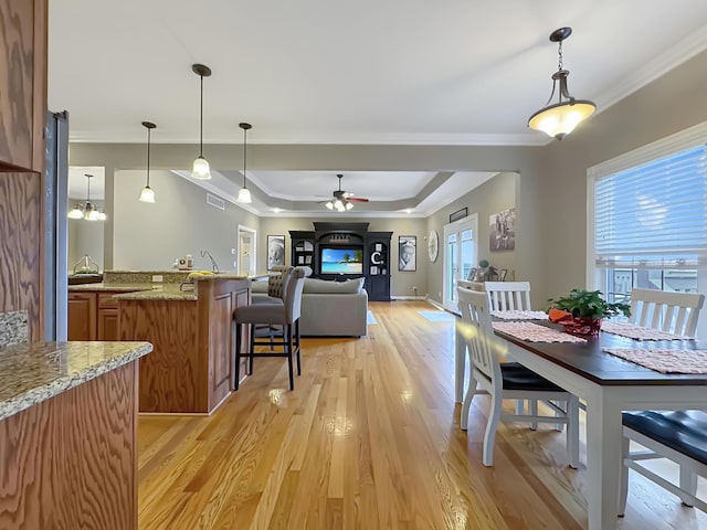 dining room featuring a raised ceiling, crown molding, ceiling fan, and light hardwood / wood-style flooring