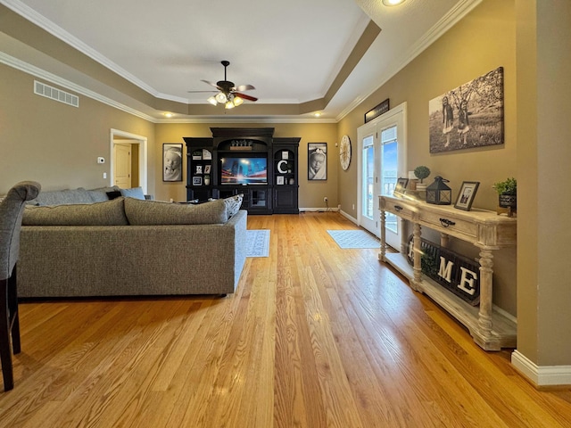 living room with crown molding, ceiling fan, a tray ceiling, light hardwood / wood-style floors, and french doors