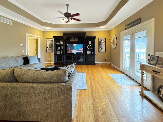 living room featuring a tray ceiling, ornamental molding, ceiling fan, and light wood-type flooring