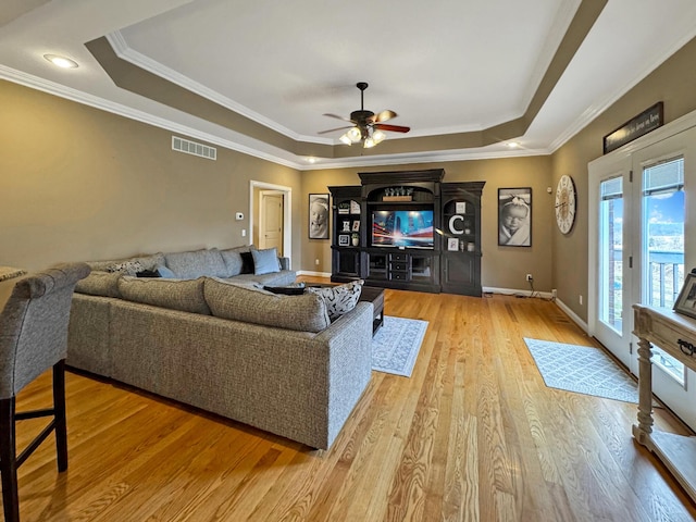 living room featuring ceiling fan, ornamental molding, a raised ceiling, and light hardwood / wood-style flooring