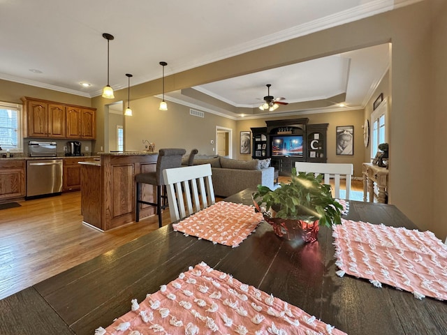 dining space with a tray ceiling, ornamental molding, ceiling fan, and light wood-type flooring