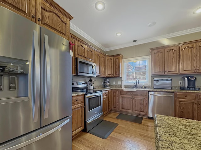 kitchen featuring sink, ornamental molding, pendant lighting, stainless steel appliances, and light stone countertops