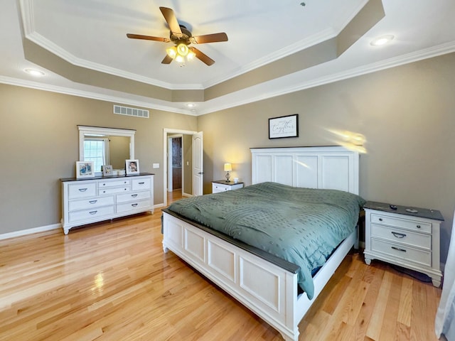 bedroom with ceiling fan, ornamental molding, a raised ceiling, and light hardwood / wood-style floors