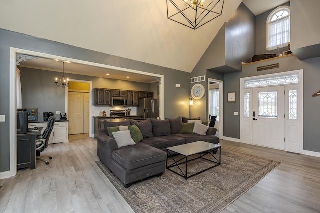 living room featuring crown molding, a high ceiling, a chandelier, and light wood-type flooring