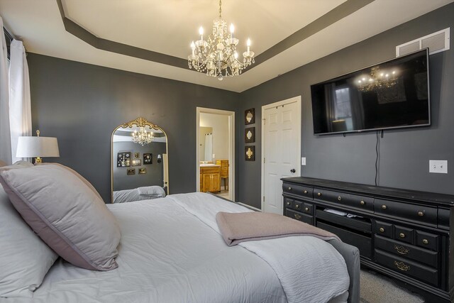 bedroom with ensuite bath, a tray ceiling, and a notable chandelier