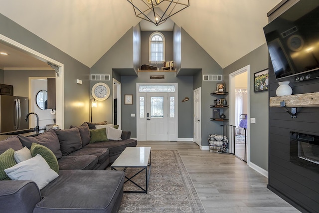 living room featuring high vaulted ceiling, a notable chandelier, and light hardwood / wood-style floors