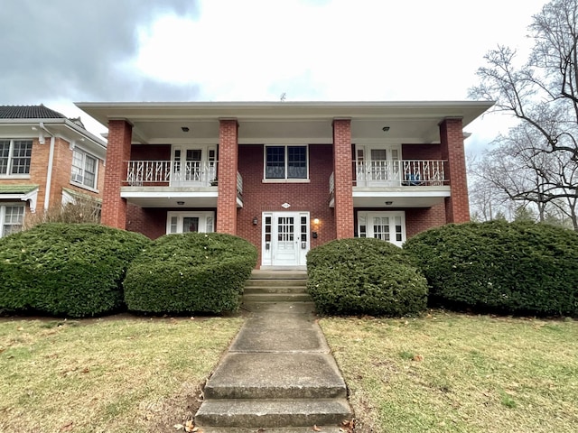 view of front of property with a balcony, a front lawn, french doors, and brick siding