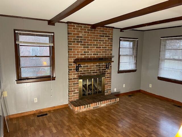 unfurnished living room featuring dark wood-type flooring, a brick fireplace, and beamed ceiling