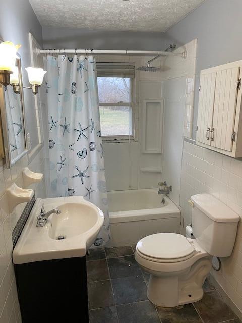 full bathroom with shower / tub combo with curtain, toilet, a textured ceiling, tile walls, and vanity