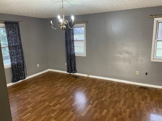 spare room featuring dark wood-type flooring, a notable chandelier, and a textured ceiling