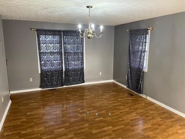 unfurnished room with dark wood-type flooring, a chandelier, and a textured ceiling