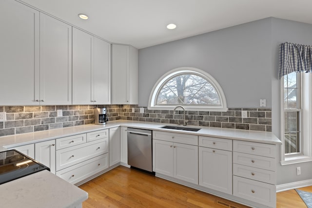 kitchen with tasteful backsplash, white cabinetry, sink, stainless steel dishwasher, and light hardwood / wood-style floors