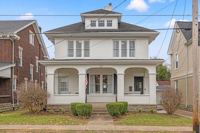 american foursquare style home with covered porch, brick siding, and a chimney