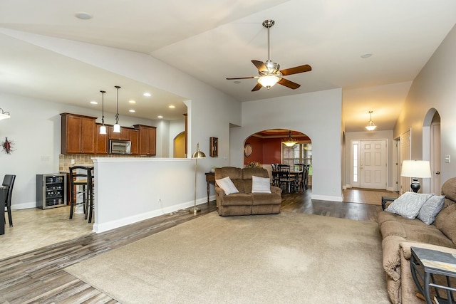 living room with arched walkways, wine cooler, baseboards, vaulted ceiling, and dark wood-style floors