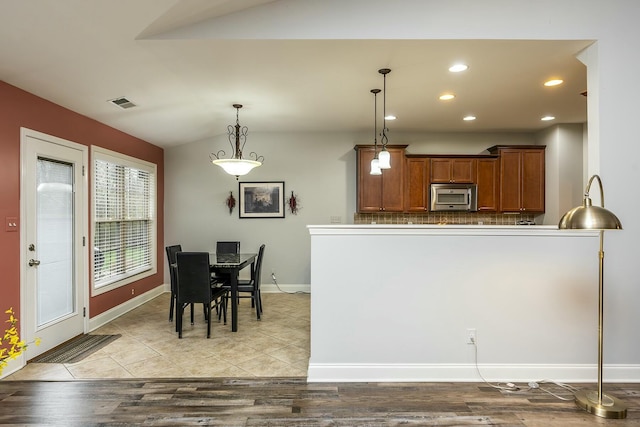 kitchen with visible vents, brown cabinetry, stainless steel microwave, vaulted ceiling, and pendant lighting