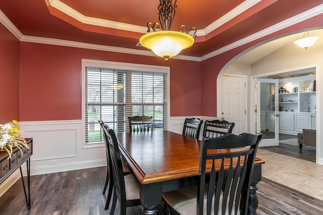 dining area featuring a wainscoted wall, arched walkways, dark wood finished floors, and ornamental molding