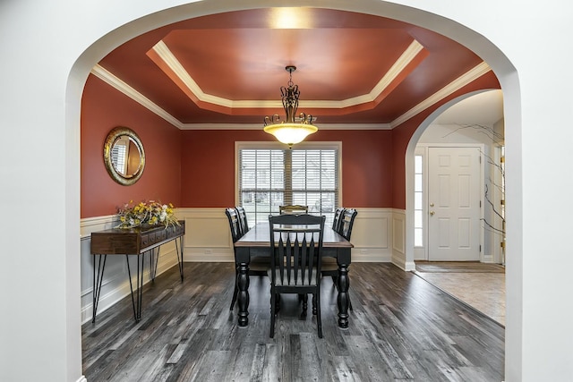 dining space featuring dark wood-style floors, crown molding, a raised ceiling, and a wainscoted wall