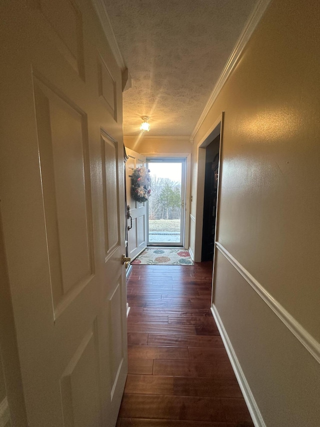 corridor featuring a textured ceiling, ornamental molding, dark wood finished floors, and baseboards