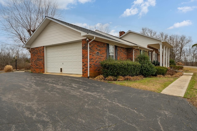 view of side of property with aphalt driveway, brick siding, a chimney, and an attached garage