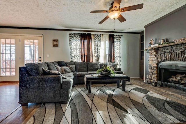 living room featuring a brick fireplace, a textured ceiling, ornamental molding, ceiling fan, and hardwood / wood-style floors