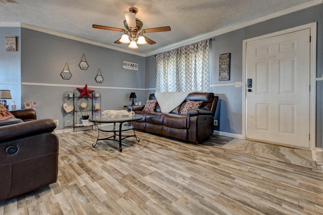 living room featuring ceiling fan, ornamental molding, a textured ceiling, and light wood-type flooring