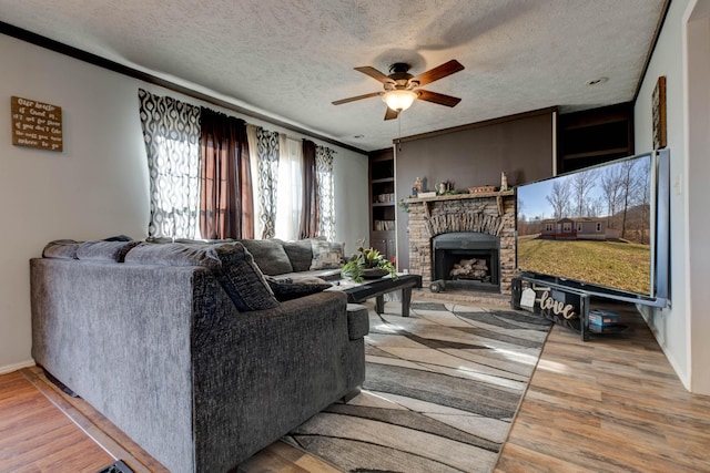 living room with ceiling fan, a textured ceiling, a fireplace, and light wood-type flooring