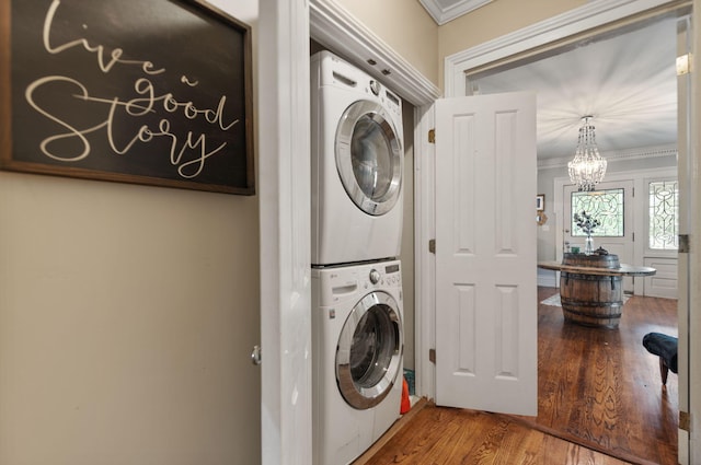 clothes washing area with crown molding, stacked washer / drying machine, an inviting chandelier, and hardwood / wood-style flooring