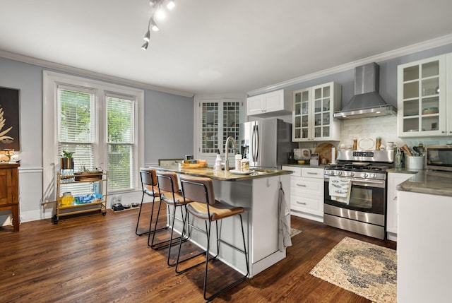 kitchen with stainless steel appliances, crown molding, white cabinets, and wall chimney exhaust hood