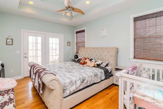 bedroom featuring baseboards, a raised ceiling, access to exterior, light wood-style floors, and recessed lighting