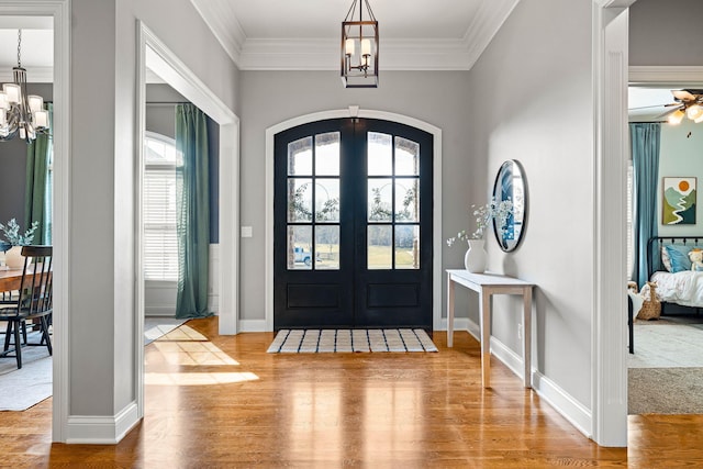 foyer entrance with wood-type flooring, ornamental molding, french doors, and a chandelier