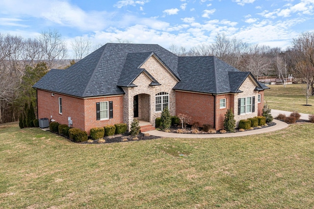 french country inspired facade with a shingled roof, a front lawn, central AC, and brick siding