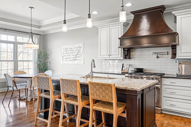 kitchen featuring sink, a tray ceiling, white cabinets, and premium range hood