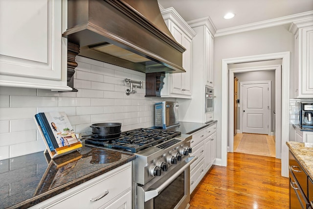 kitchen with white cabinetry, backsplash, stainless steel appliances, custom exhaust hood, and light wood-type flooring