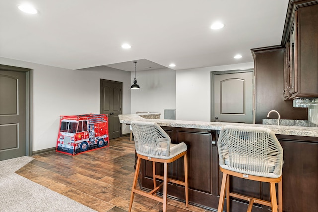 kitchen featuring hanging light fixtures, dark brown cabinets, a kitchen breakfast bar, dark hardwood / wood-style floors, and light stone countertops