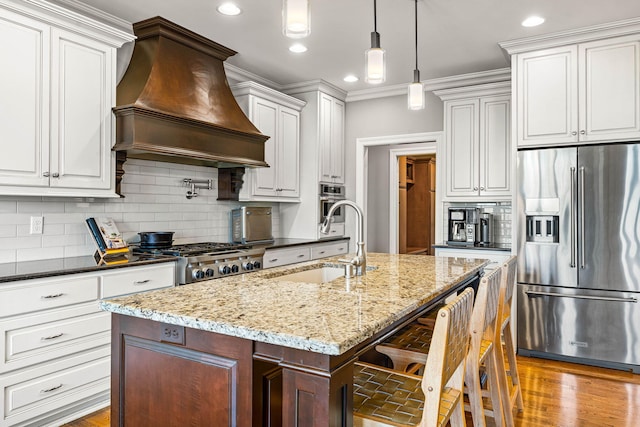 kitchen with appliances with stainless steel finishes, a breakfast bar, sink, custom exhaust hood, and hanging light fixtures