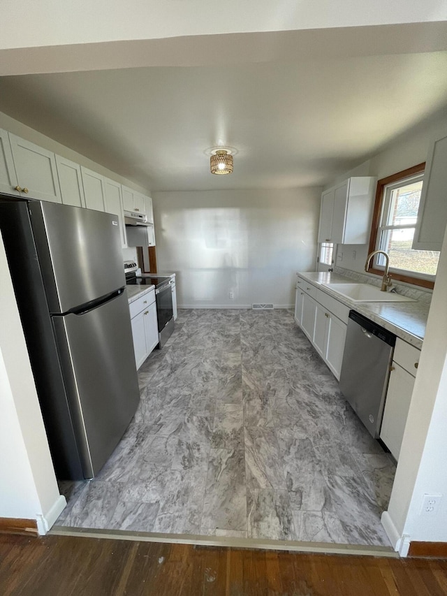 kitchen with appliances with stainless steel finishes, sink, white cabinets, and light hardwood / wood-style floors