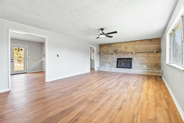 unfurnished living room with a fireplace, light hardwood / wood-style floors, a textured ceiling, and plenty of natural light