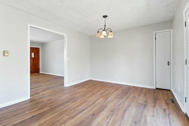 unfurnished room featuring a notable chandelier, a textured ceiling, and light hardwood / wood-style floors