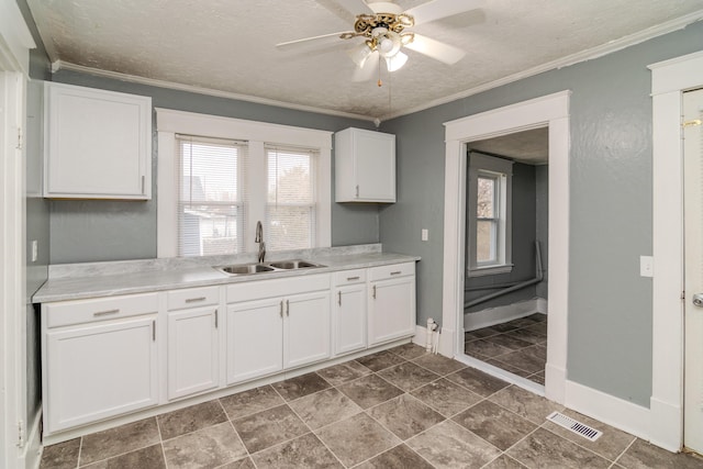 kitchen with sink, ceiling fan, white cabinetry, ornamental molding, and a textured ceiling