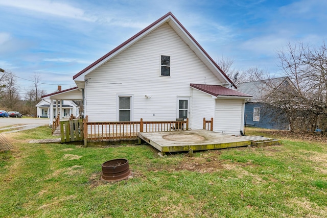 back of property with an outdoor fire pit, a deck, and a lawn