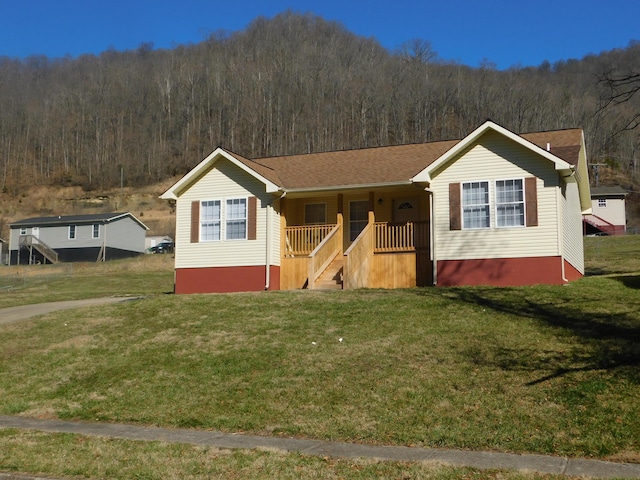 ranch-style house with covered porch, a forest view, and a front yard