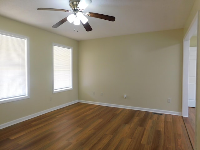 spare room with dark wood-type flooring, visible vents, ceiling fan, and baseboards